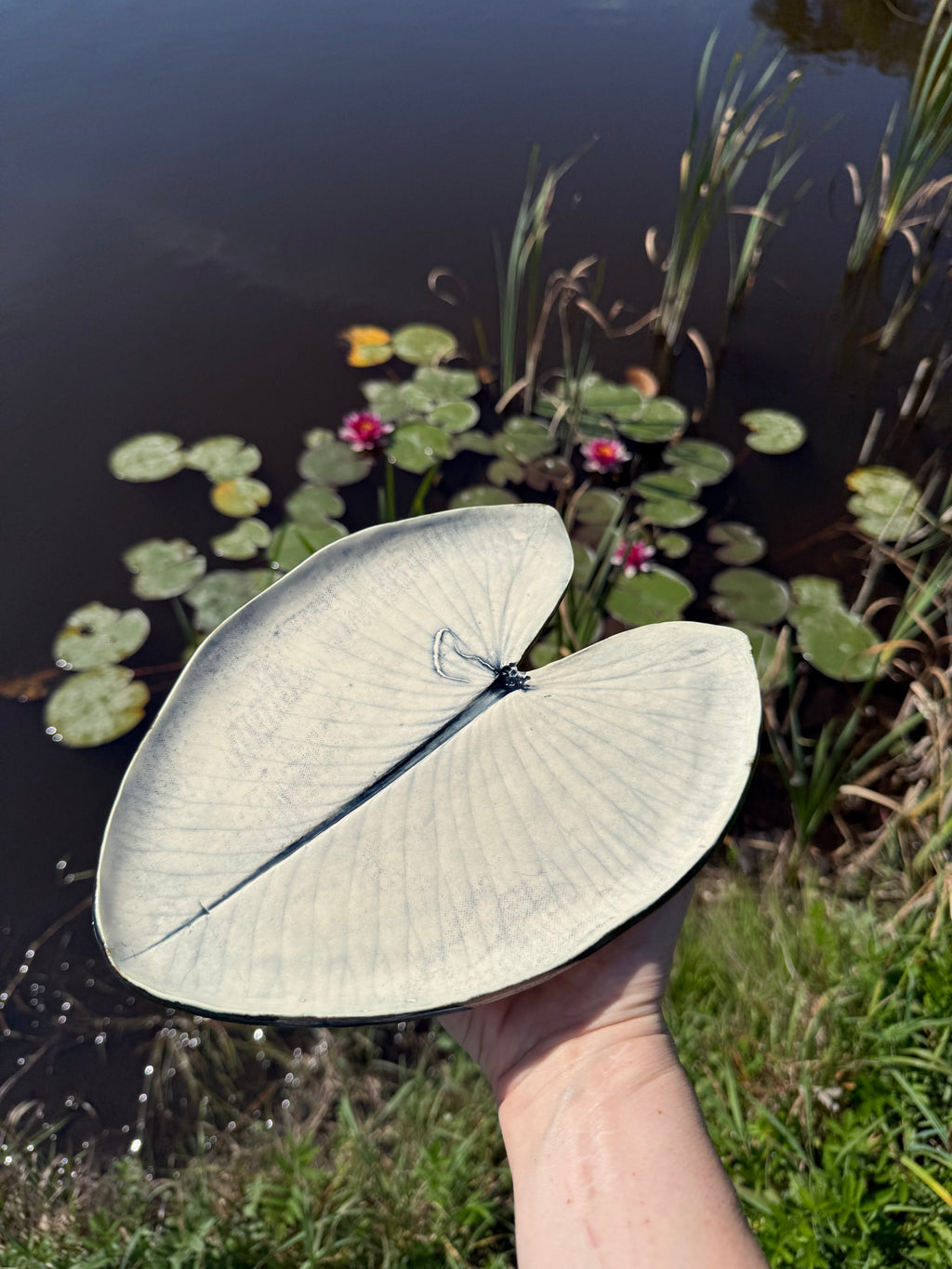 Rankų darbo keraminė lėkštė Lelijos lapas laikoma rankoje